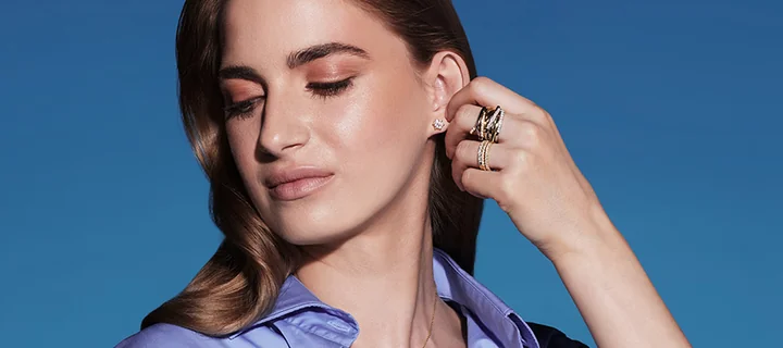 Kobieta z zamkniętymi oczami dotyka ucha; widać kolczyk, kilka pierścionków i błękitną koszulę