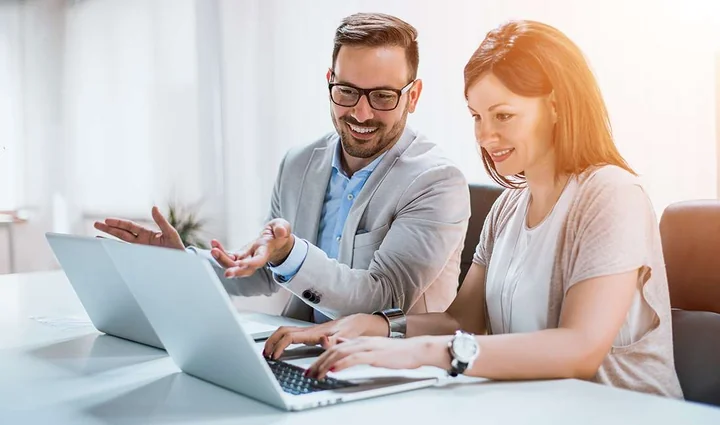 Zdjęcie przedstawia kobiete i mężczyzne podczas pracy przy laptopach