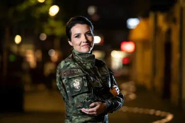 Funkcjonariuszka Straży Granicznej w mundurze bojowym pozuje do zdjęcia na oświetlonej ulicy nocą.
