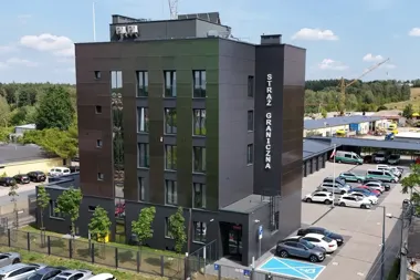 Nowoczesny, wielokondygnacyjny budynek siedziby Straży Granicznej z parkingiem i pojazdami służbowymi w otoczeniu zabudowy przemysłowej.